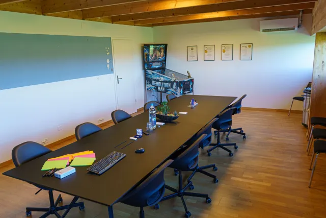 Sitzungszimmer mit langem Tisch, Auszeichnungen an der Wand und einem Flipperautomaten